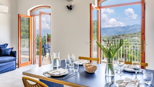 Un coin repas avec une table dressée pour deux personnes, un canapé bleu et une vue sur les montagnes à travers de grandes fenêtres.