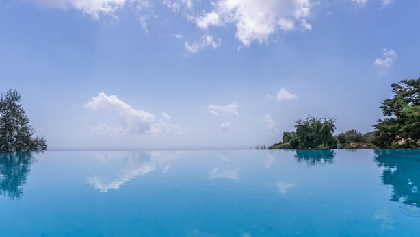 A clear blue infinity pool with a view of the ocean and distant trees under a partly cloudy sky. - Le Arcate Giuliana in Massa Lubrense (Massa Lubrense)