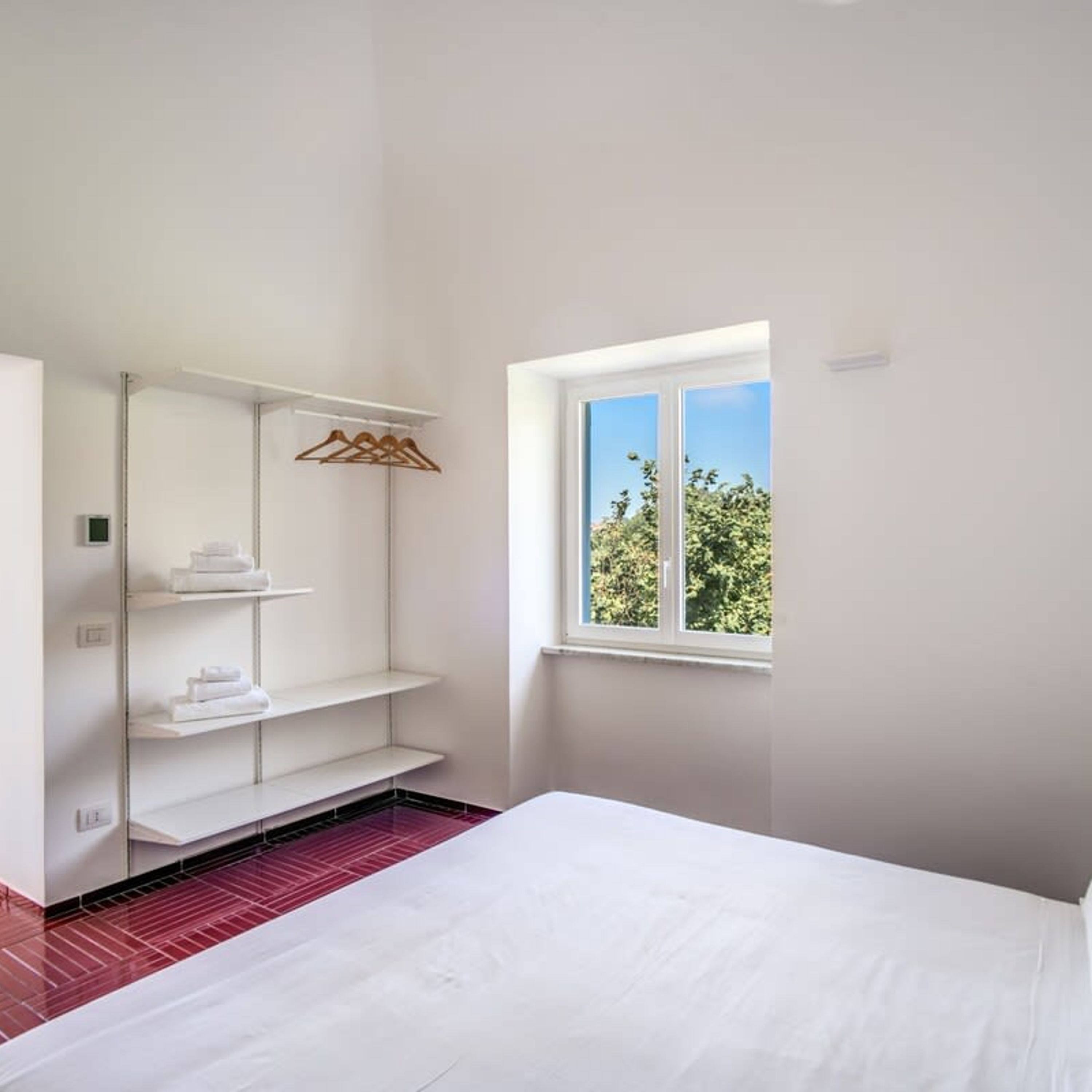 A bedroom with a bed, a window, and a built-in wardrobe with shelves.