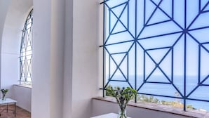 Une pièce dotée d’une grande fenêtre aux motifs géométriques, d’une table blanche et d’une chaise en métal.