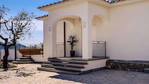 A building with a white facade, a tiled patio, and a tree in the foreground. - Villa Rusinella in Massa Lubrense (Massa Lubrense)