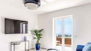 A modern living room with a flat-screen TV, a potted plant, a sofa, and a sliding glass door leading to an outdoor area. - Villa Rusinella in Massa Lubrense (Massa Lubrense)