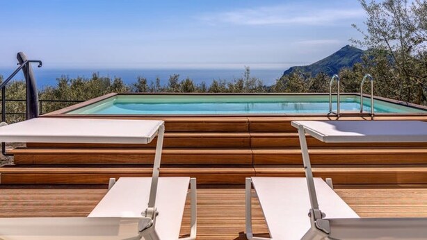 A poolside area with wooden decking, two white lounge chairs, and a view of the ocean and mountains. - Villa Rusinella in Massa Lubrense (Massa Lubrense)