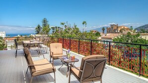 Una terraza con mobiliario exterior, una cerca decorativa y vistas a edificios y al mar.