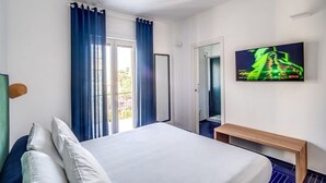 Habitación de hotel con cama, un banco, televisión y vistas al balcón.
