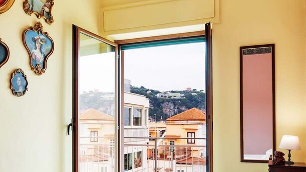 A hotel room with two beds, a large window with a city view, and a wall with framed artwork. - La Musica in Sorrento (Sorrento)