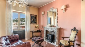 A living room with a fireplace, a leather sofa, a patterned armchair, and a view of the outdoors. - La Musica in Sorrento (Sorrento)