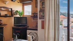A cozy living room with a TV, a dining table with chairs, a coffee maker, and a plant. There is a balcony with a view of buildings and hills. - La Musica in Sorrento (Sorrento)