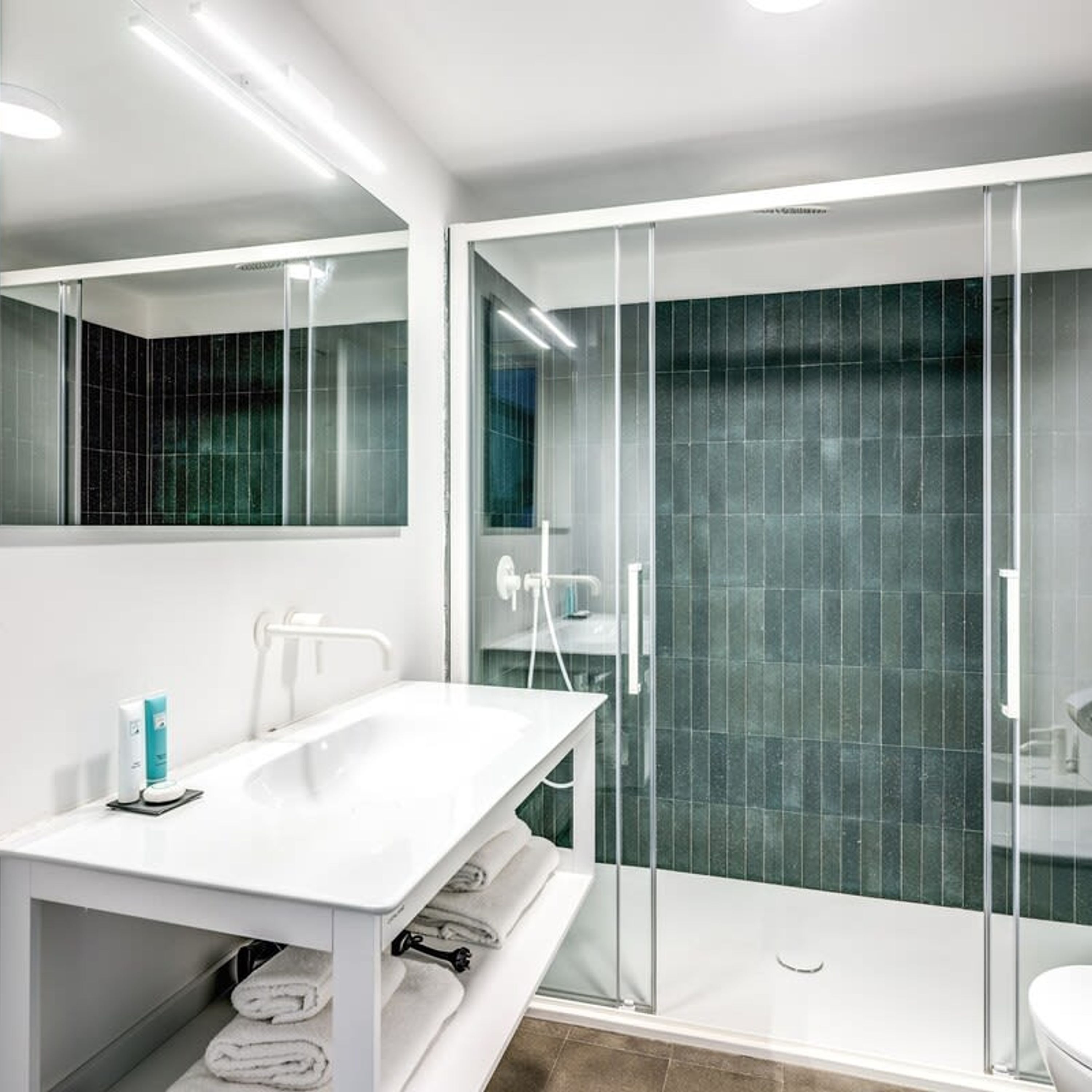A modern bathroom with a white vanity, a glass shower enclosure, and a dark tiled shower wall.