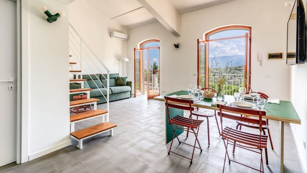 Un vaste espace de vie comprenant un coin repas avec une table pour quatre personnes, un escalier et une vue sur l’extérieur.