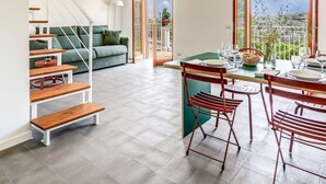 Un vaste espace de vie comprenant un escalier, une table à manger pour quatre personnes et une vue sur l’extérieur grâce à de grandes fenêtres.