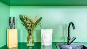 Un plan de travail de cuisine avec un mur vert, un évier, un bloc à couteaux, un vase contenant des plantes séchées et un sac étiqueté « NETTOYAGE – L’ESPRIT DE L’ITALIE ».