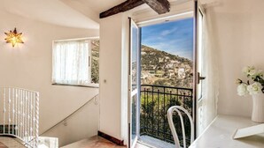 Una habitación con balcón, una lámpara con forma de estrella, una silla blanca y una mesa con un jarrón de flores.