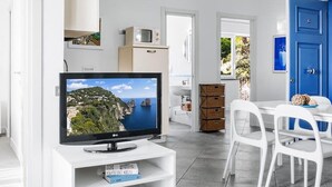 Een moderne woonkamer met een flatscreen televisie, witte meubels en uitzicht op een kustlandschap.