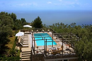 Une piscine sur le toit offrant une vue dégagée sur la mer, entourée de chaises longues et de parasols.