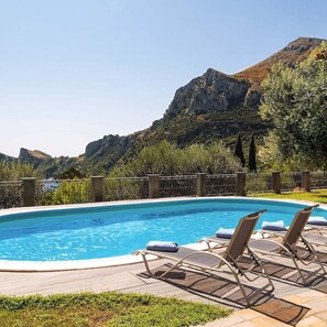 A swimming pool with lounge chairs, surrounded by a wooden deck and a metal fence, with mountains in the background. - Relais Mamma Mia in Nerano (Massa Lubrense)