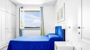 Een slaapkamer met een bed, een raam met gordijnen, een nachtkastje en een wandlamp.