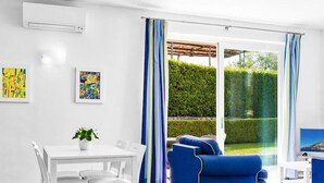 Een moderne woonkamer met een witte tafel en stoelen, een blauwe bank en een grote schuifpui die uitkomt op een tuin.