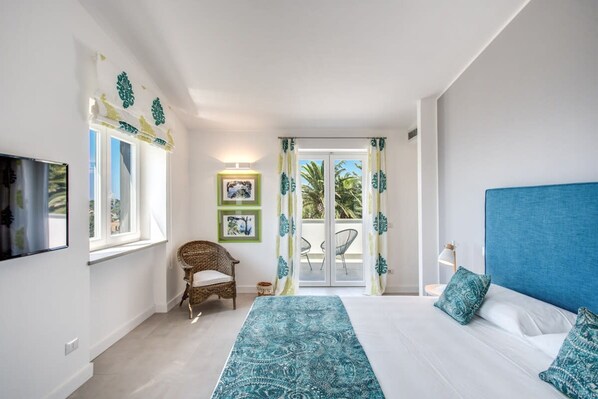 A bedroom with a bed, a chair, a TV, and a balcony with curtains.