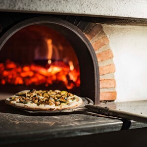 Pizza in een bakstenen oven met zichtbaar vuur.