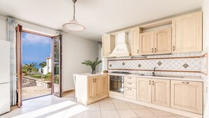 A modern kitchen with light wood cabinets, a central island, and a view of the outdoors. - Villa Mimosa in Massa Lubrense (Massa Lubrense)