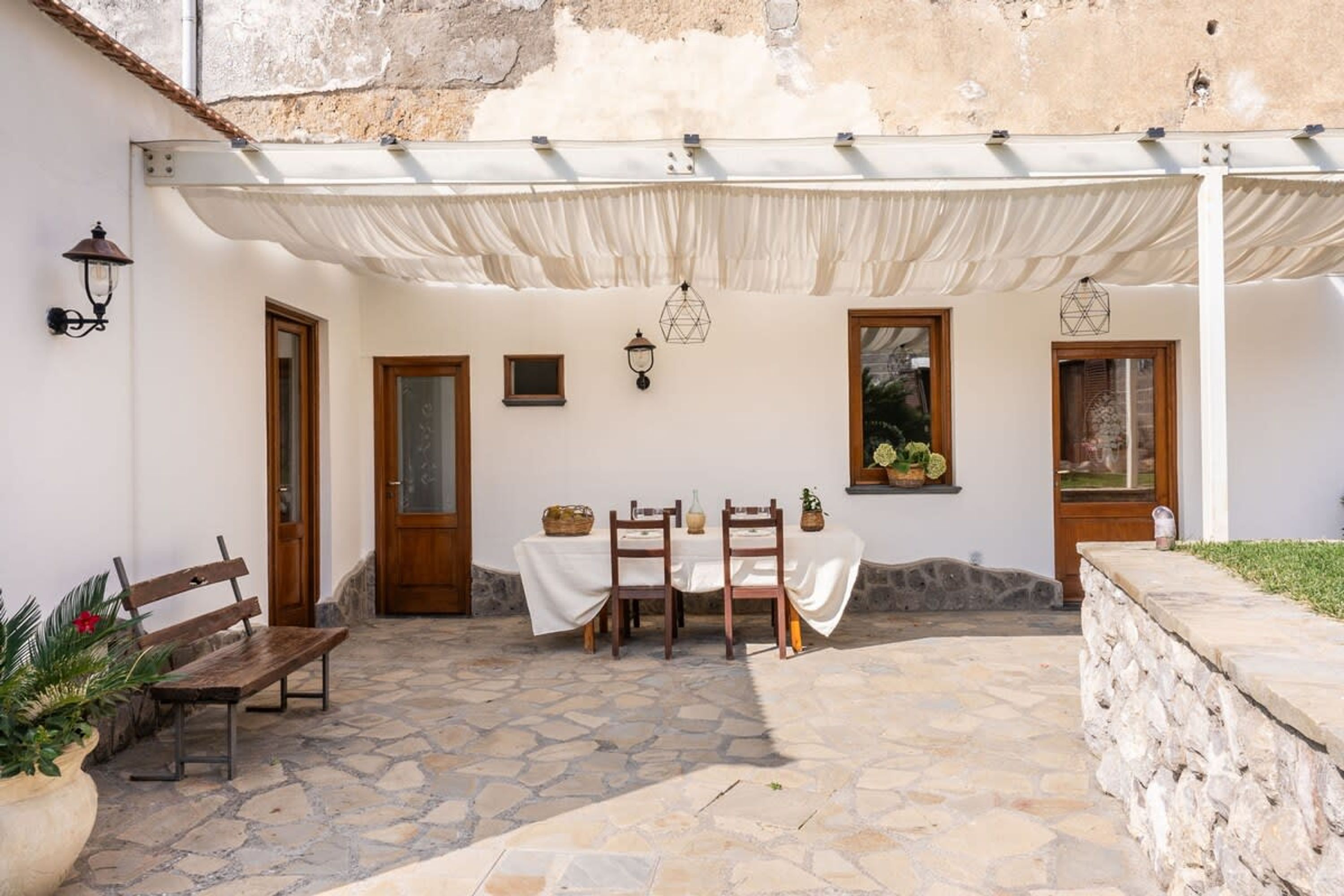 An outdoor patio with a table set for two, a bench, and a covered seating area.