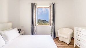 A bedroom with a bed, a nightstand, a chair, a dresser, and a window with curtains. - Villa Mimosa in Massa Lubrense (Massa Lubrense)