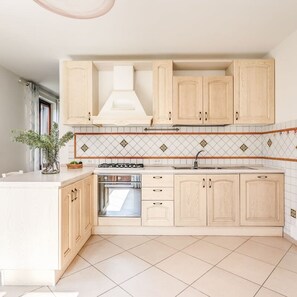 Een moderne keuken met lichte houten kastjes, een centraal eiland, een inbouwoven en een betegelde spatwand.