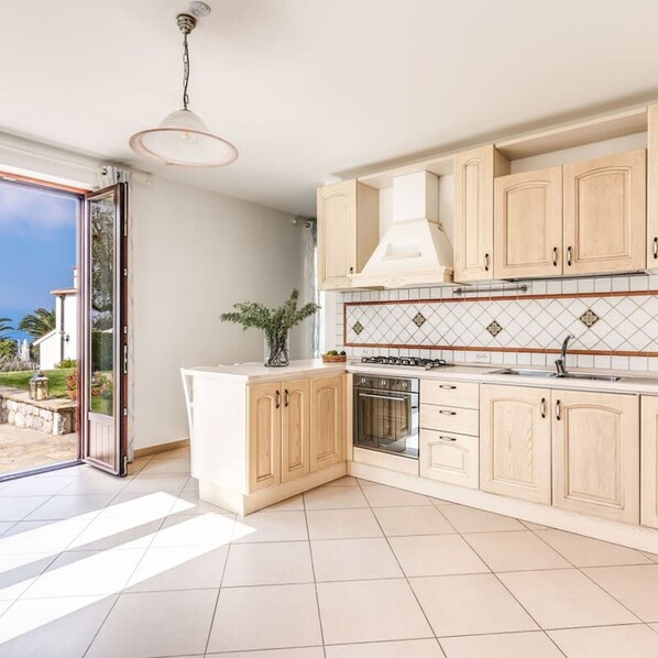 Een moderne keuken met lichte houten kastjes, een centraal eiland, een inbouwoven en een groot raam.