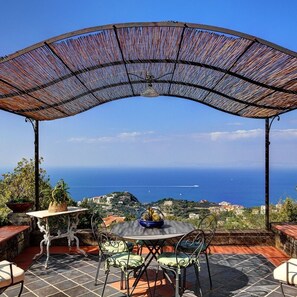 A covered outdoor seating area with a table and chairs, overlooking a coastal view. - Fondo Turiello in Massa Lubrense (Massa Lubrense)