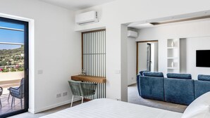 Une chambre d’hôtel moderne dotée d’un grand lit, d’un balcon avec coin salon extérieur, d’un bureau avec une chaise et d’un espace détente avec un canapé.