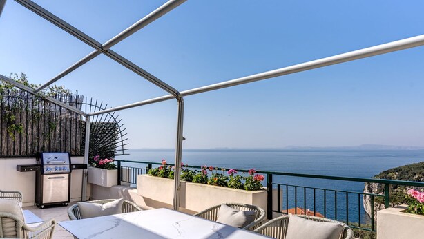 Une terrasse avec une table blanche et des chaises en osier, offrant une vue sur la côte.