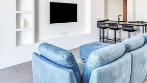 Un salon moderne avec un téléviseur à écran plat fixé au mur, un coin repas avec un bar et une cuisine en arrière-plan.