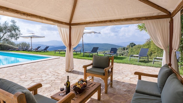 A covered outdoor seating area with a pool, lounge chairs, and a table with a bottle and fruit bowl. - Apartment in Farm with pool (Gambassi Terme)