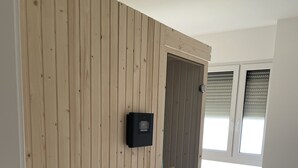 A room with a wooden wardrobe, a thermostat, and a window with blinds.
