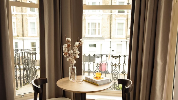 Een hotelkamer met balkon, een ronde tafel met twee stoelen, een vaas met bloemen en een boek.
