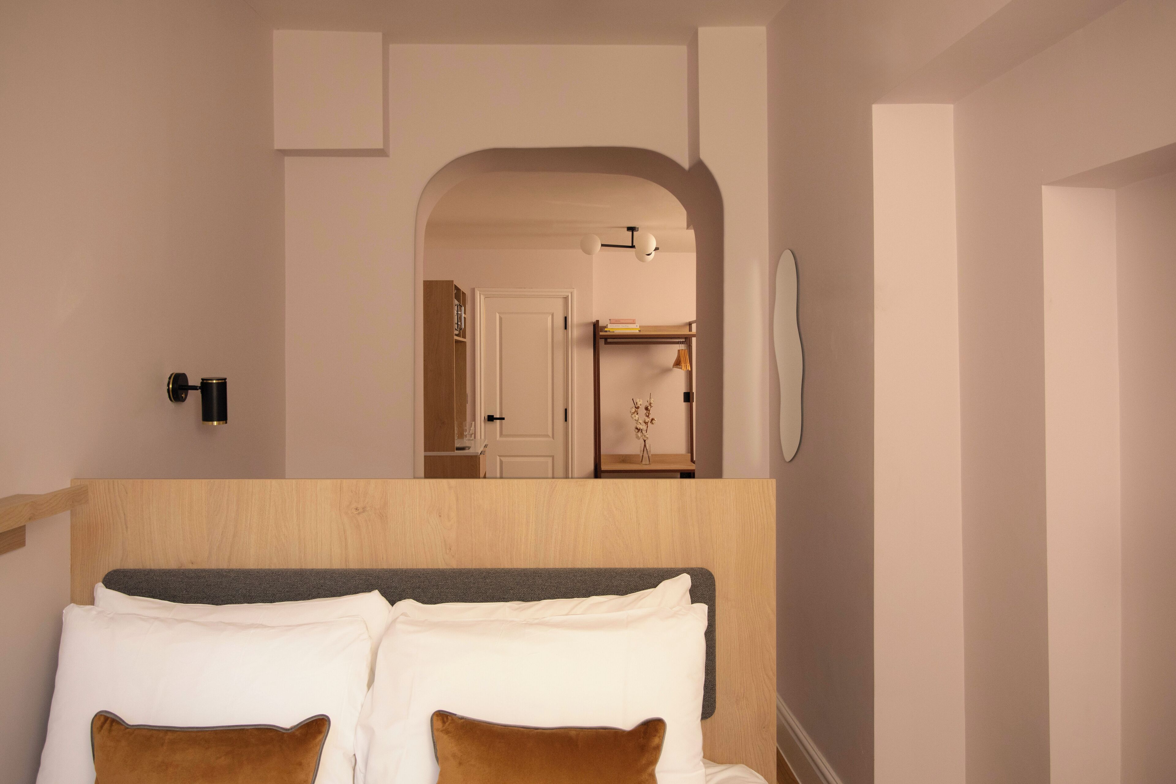 Een slaapkamer met een houten hoofdbord, wit beddengoed en een spiegel aan de muur.