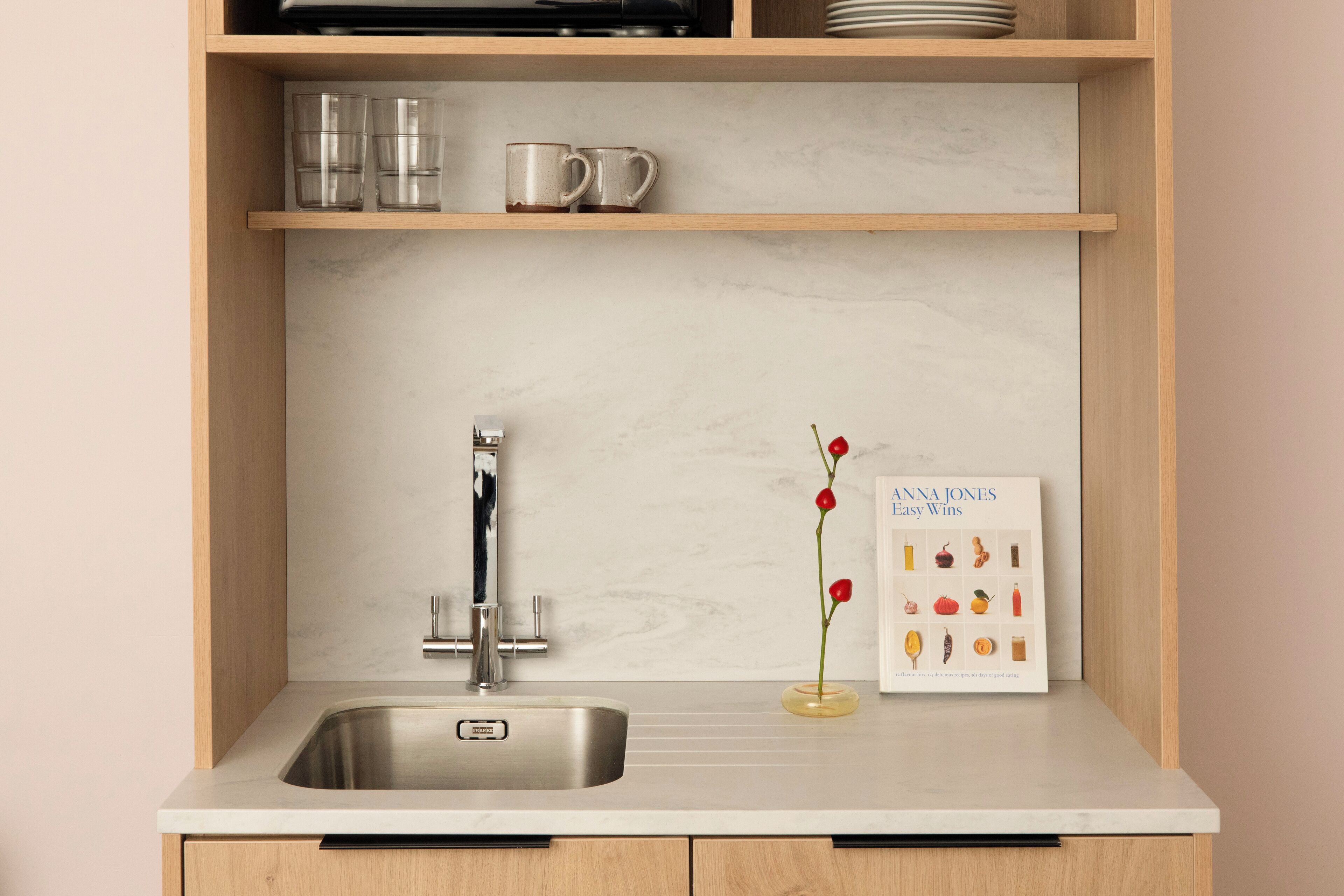 Cozinha com pia de aço inoxidável, armários de madeira e painel de backsplash de mármore.
