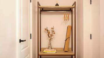 A wooden shelf unit with a vase of dried flowers, a rolled-up mat, and a pair of slippers.