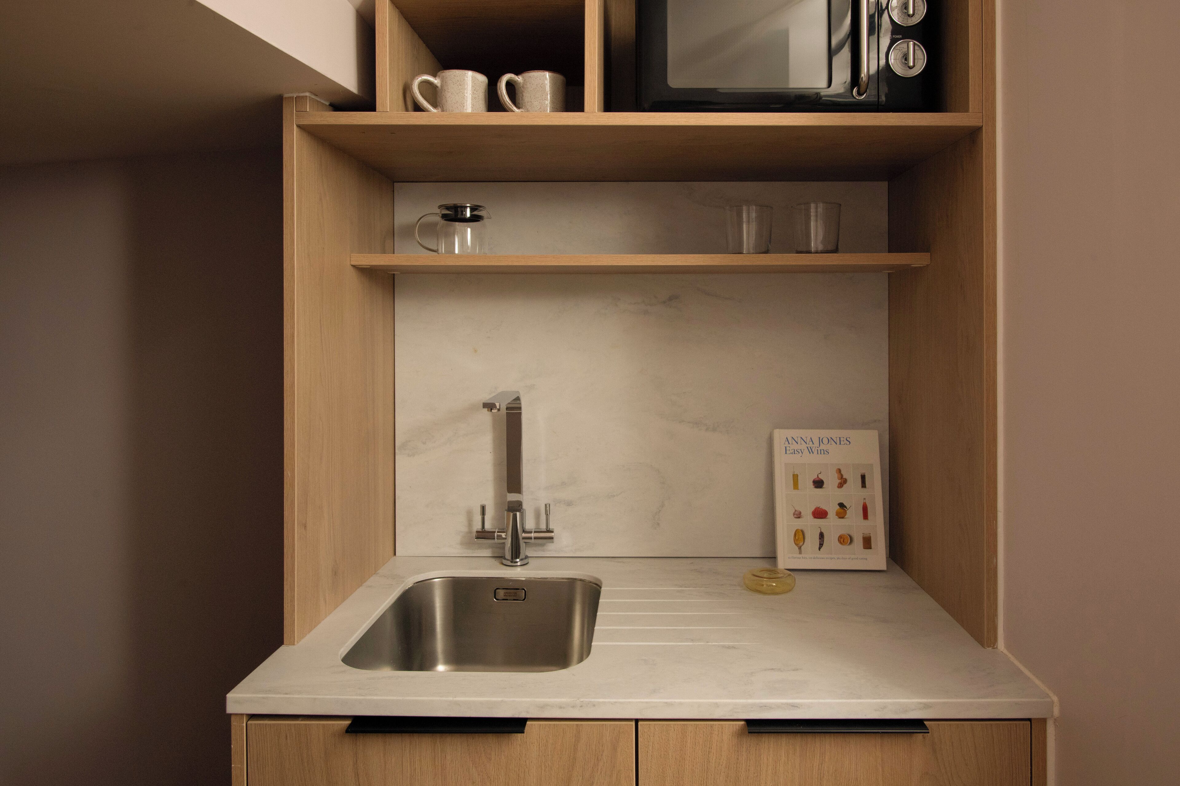 A compact kitchen with a sink, a microwave, and a coffee maker on a shelf.