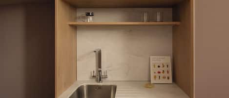 A compact kitchen with a sink, a microwave, and a coffee maker on a shelf.