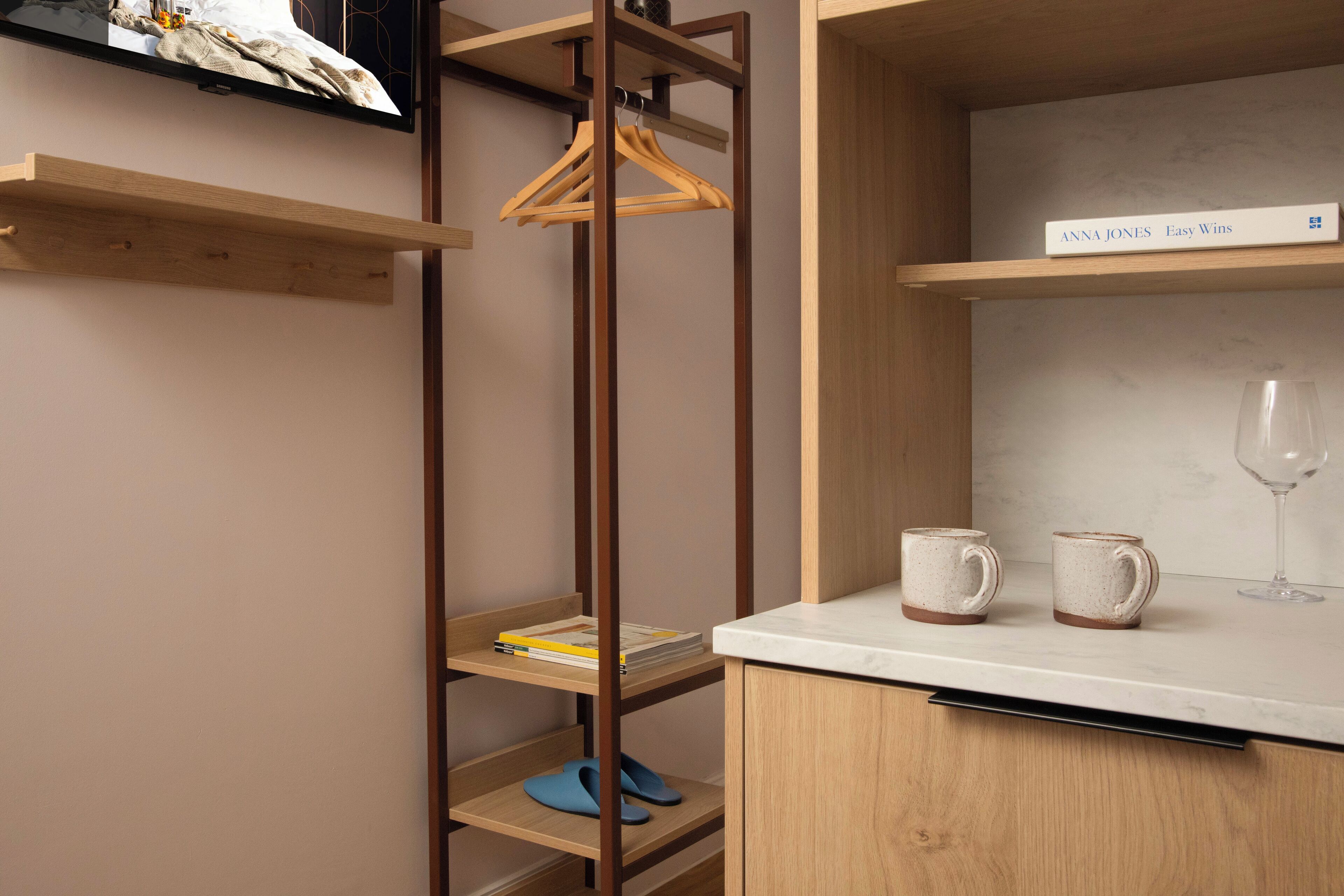 A modern kitchen with wooden shelves, a hanging rack, and a countertop with two mugs and a wine glass.