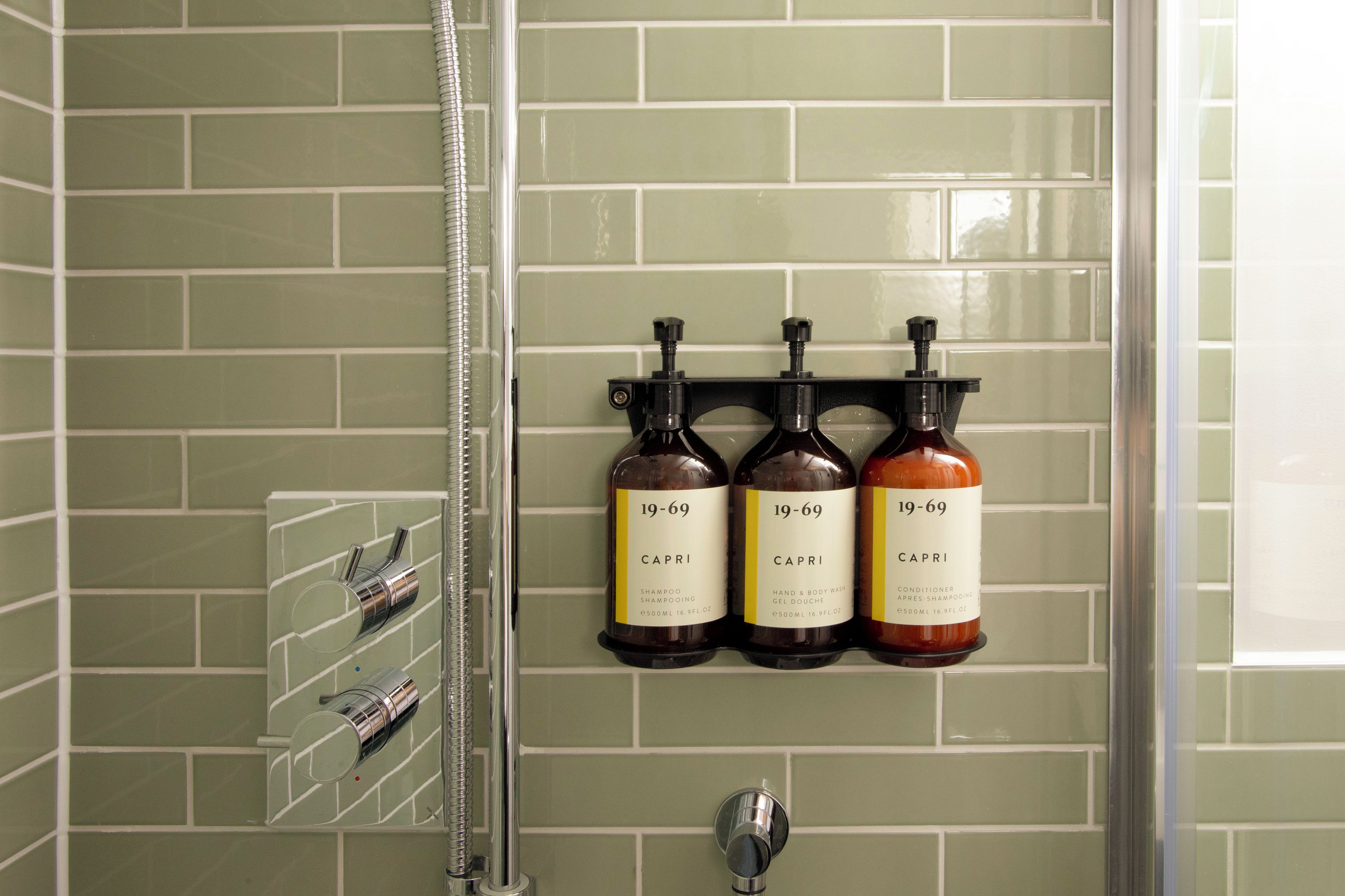 A bathroom with a shower, a glass rack holding toiletries, and three bottles of shampoo labeled 'CAPRI'.