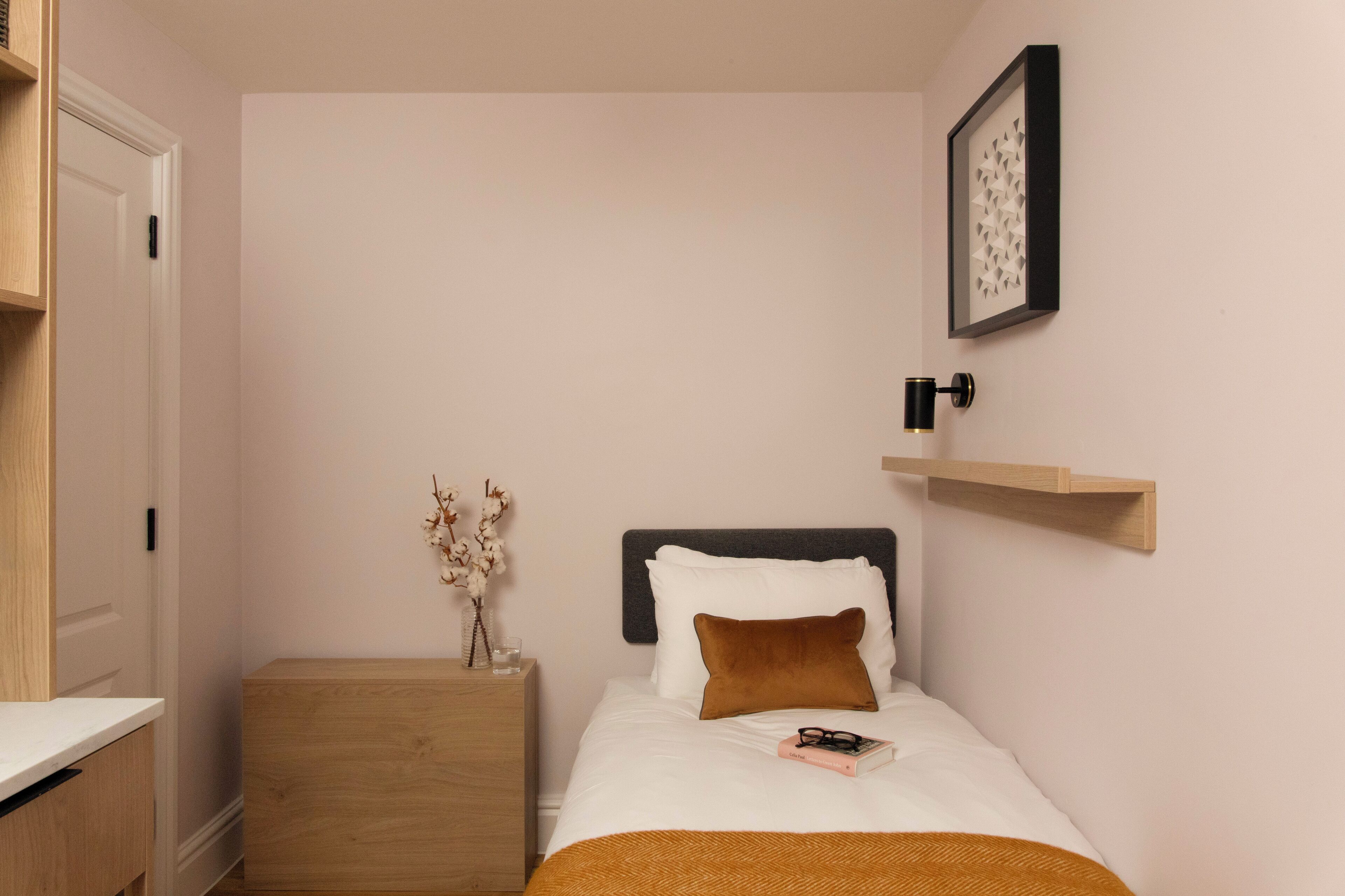 A neatly arranged bedroom with a bed, bedside table, and a wall-mounted shelf.