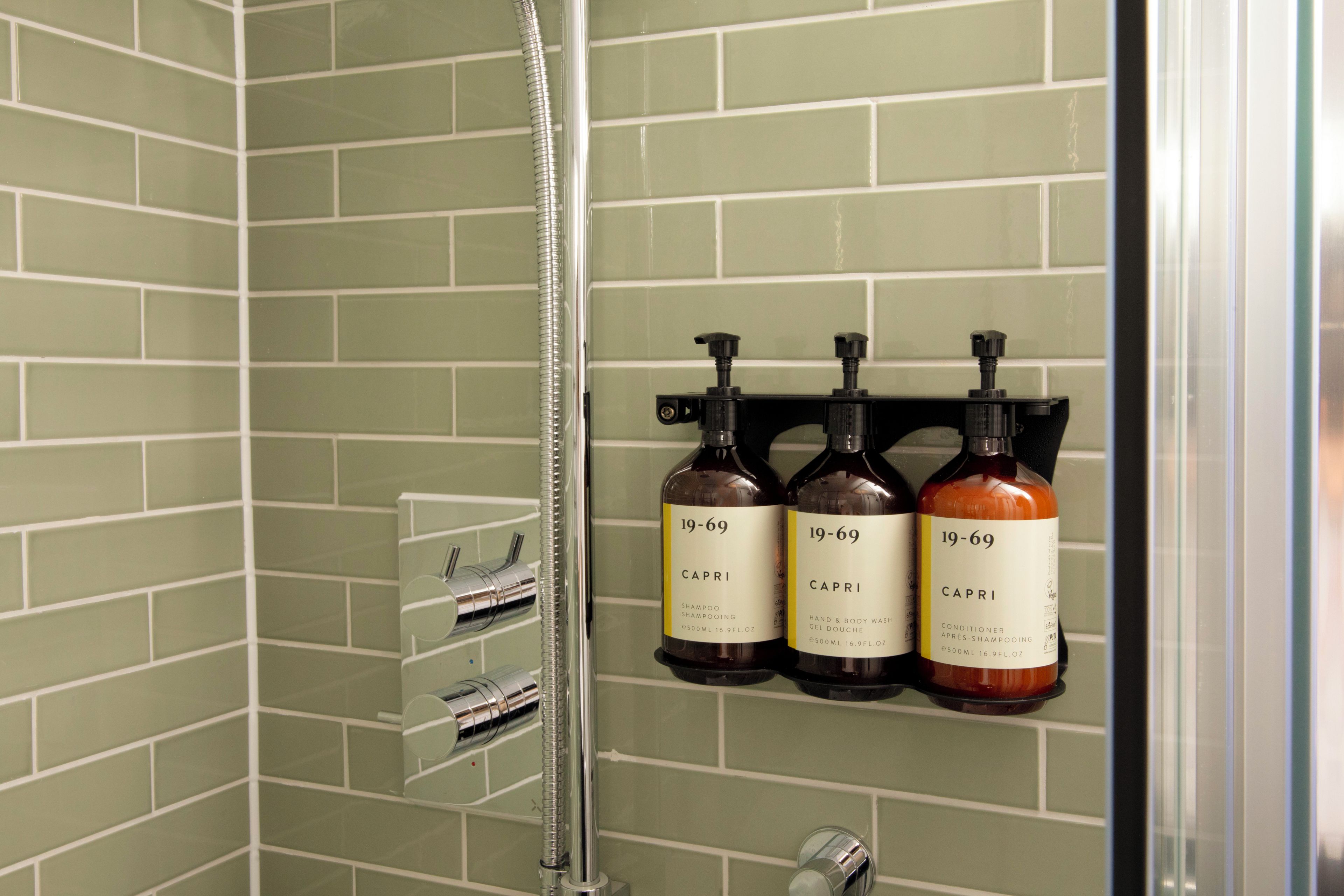 Une salle de bain avec une douche, un sèche-mains et trois bouteilles de shampoing et d’après-shampoing Capri.