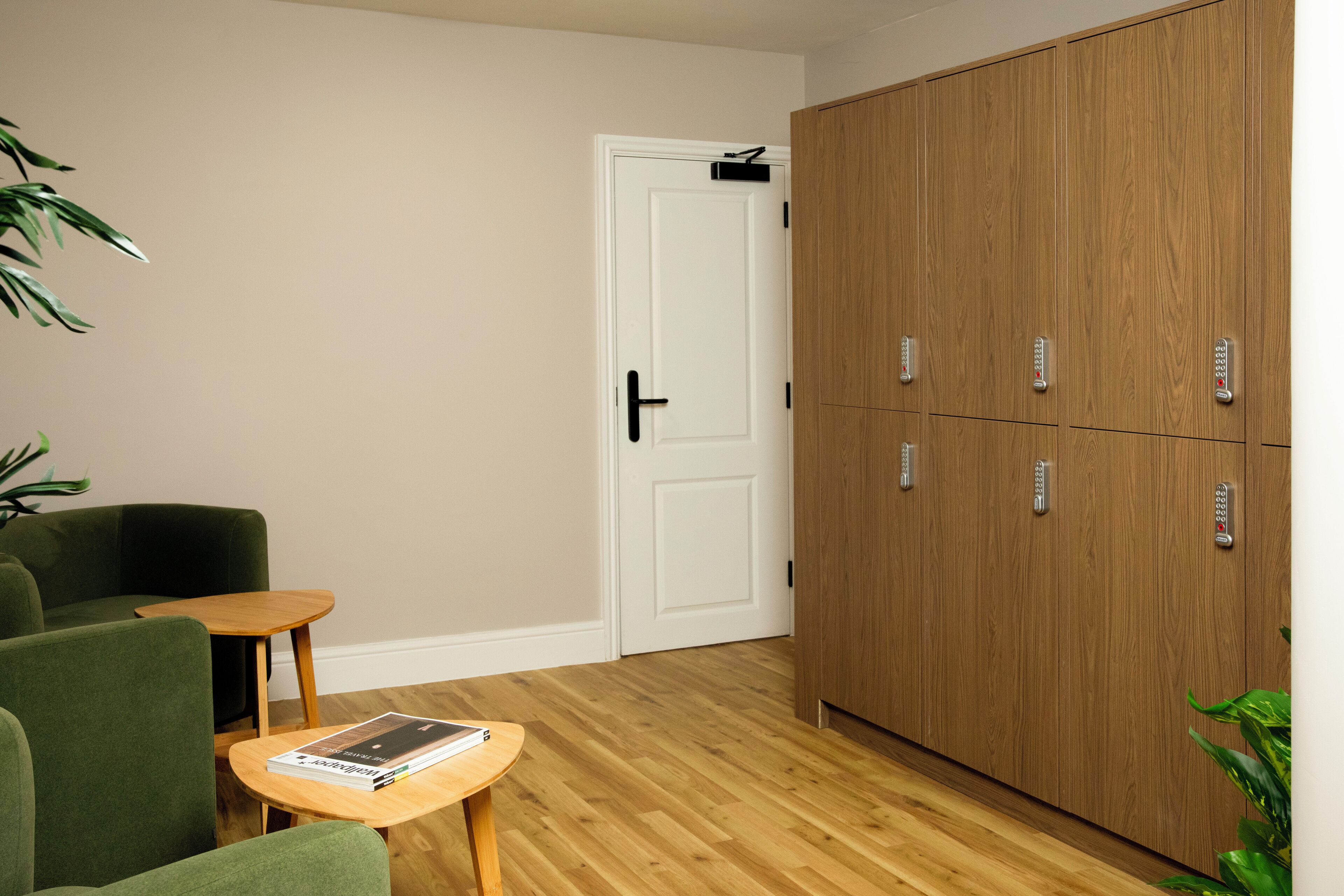 Une pièce avec un canapé vert, une petite table en bois sur laquelle repose un magazine, une porte blanche et une armoire en bois dotée de plusieurs compartiments.