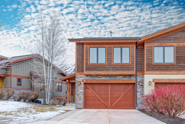 A two-story house with a garage, a stone foundation, and a wooden exterior.