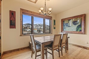 Ein Essbereich mit Holztisch und -stühlen, großen Fenstern mit Blick auf einen verschneiten Berg und einer Kristallleuchter.