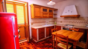 A compact kitchen with wooden cabinets, a sink, a stove, and a dining table with chairs. - Vacation home with dog boarding (Messina)