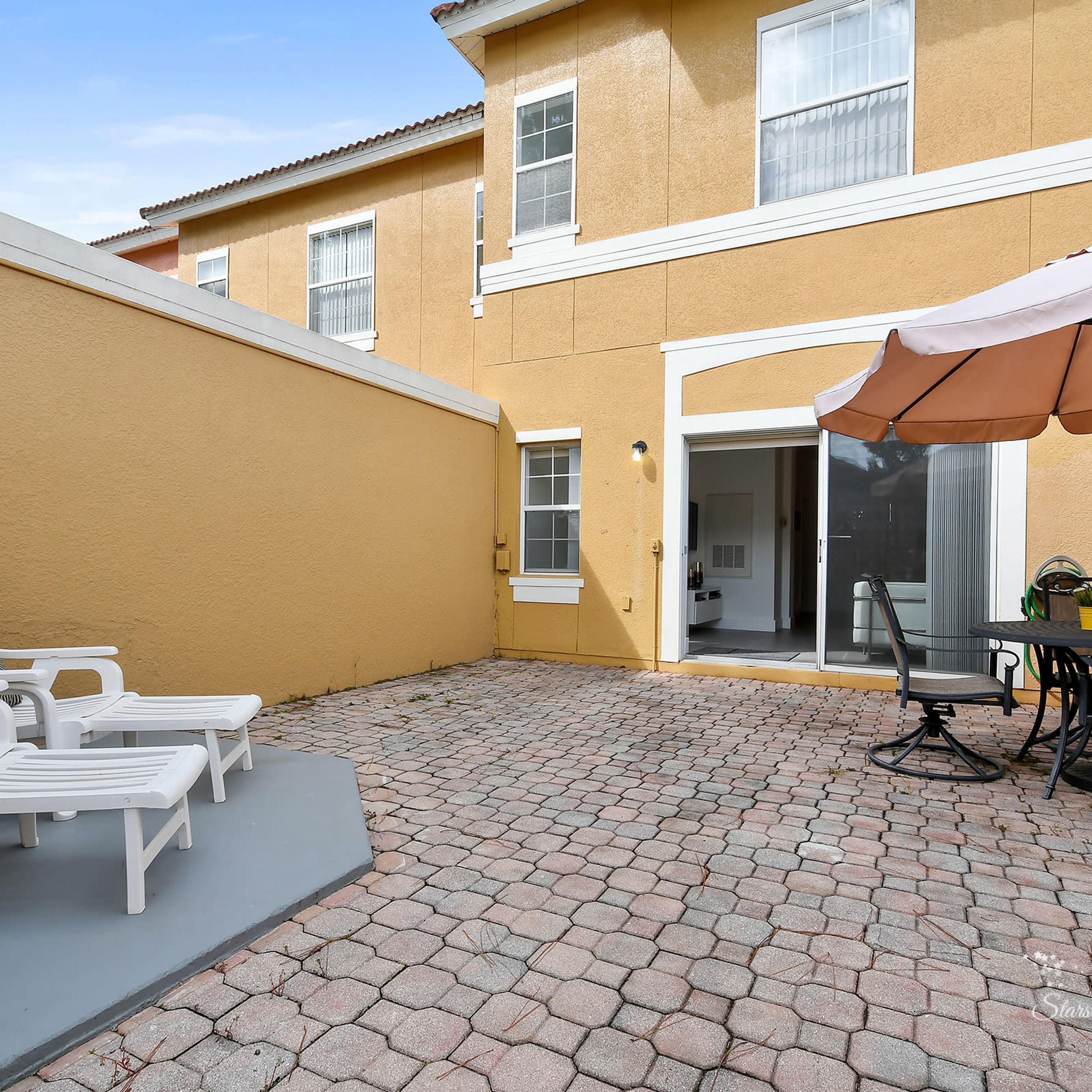 A patio with hexagonal paving, white lounge chairs, and a table with an umbrella.